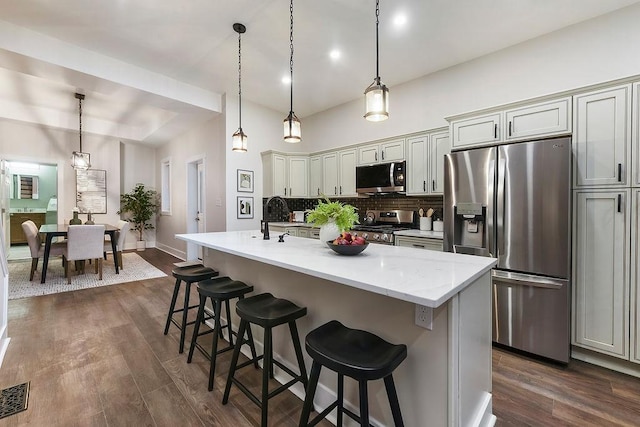 kitchen with stainless steel appliances, decorative light fixtures, an island with sink, and decorative backsplash