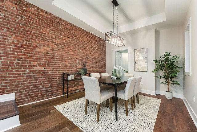 dining room featuring a raised ceiling, brick wall, and dark hardwood / wood-style floors