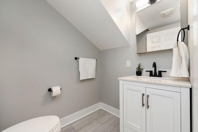 bathroom with hardwood / wood-style flooring, vanity, toilet, and vaulted ceiling