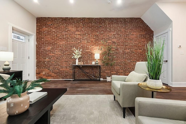 sitting room featuring hardwood / wood-style floors, vaulted ceiling, and brick wall