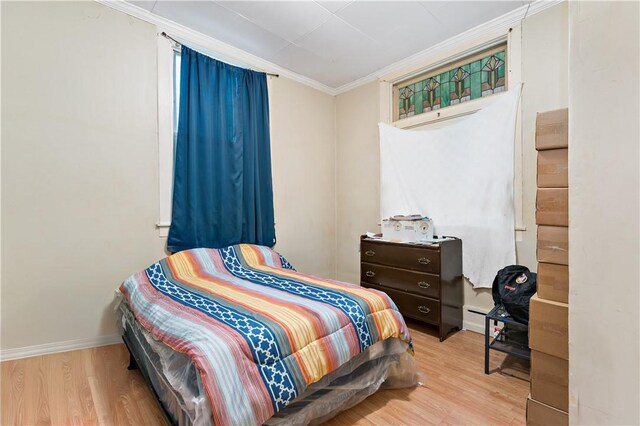 bedroom with ornamental molding, baseboard heating, and light wood-type flooring