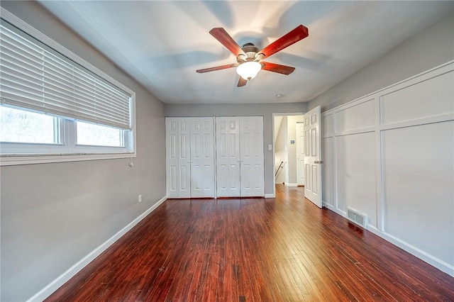 unfurnished bedroom featuring ceiling fan, dark hardwood / wood-style flooring, and two closets