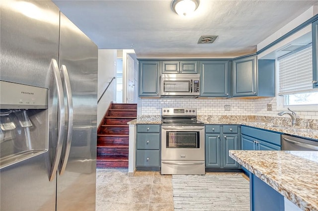 kitchen featuring light stone counters, appliances with stainless steel finishes, blue cabinetry, and backsplash