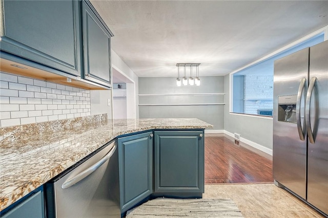 kitchen with blue cabinetry, backsplash, stainless steel appliances, light stone counters, and kitchen peninsula