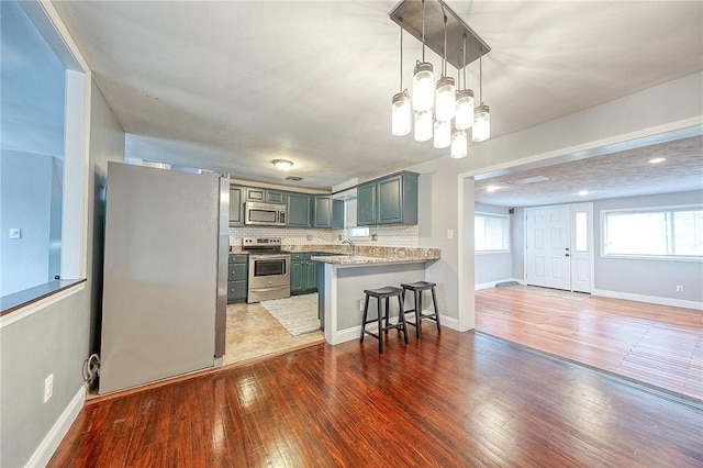 kitchen featuring appliances with stainless steel finishes, hardwood / wood-style floors, a breakfast bar area, decorative backsplash, and kitchen peninsula