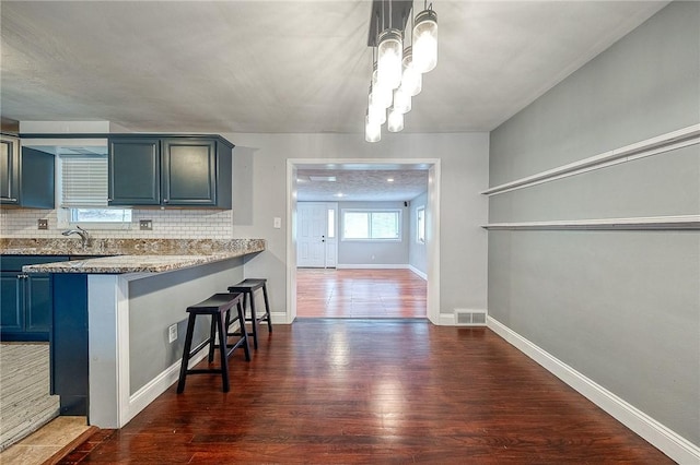 kitchen featuring tasteful backsplash, a kitchen bar, dark hardwood / wood-style flooring, and light stone countertops