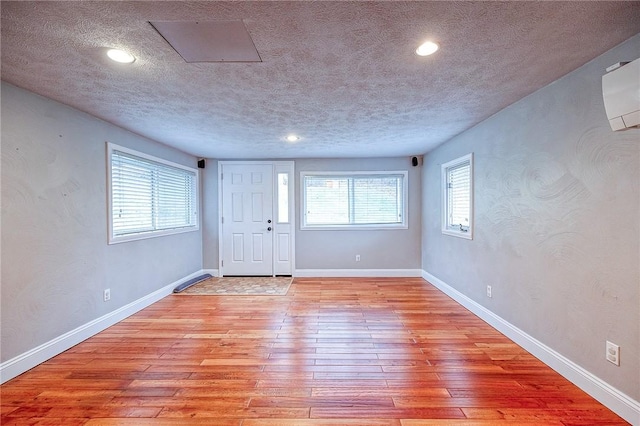 interior space with a wall unit AC, a textured ceiling, and light wood-type flooring