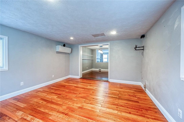 basement featuring a wall mounted air conditioner, a textured ceiling, and light hardwood / wood-style flooring