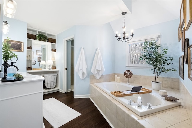 bathroom with hardwood / wood-style floors, vanity, tiled bath, vaulted ceiling, and a chandelier