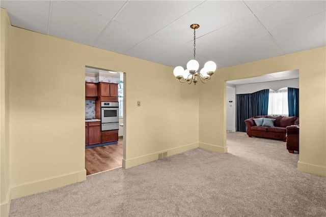 carpeted spare room featuring an inviting chandelier