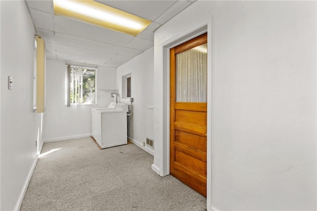 corridor featuring a paneled ceiling, light carpet, and separate washer and dryer