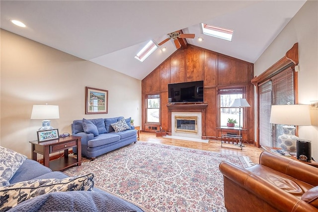 living room with a skylight, high vaulted ceiling, light wood-type flooring, a large fireplace, and ceiling fan