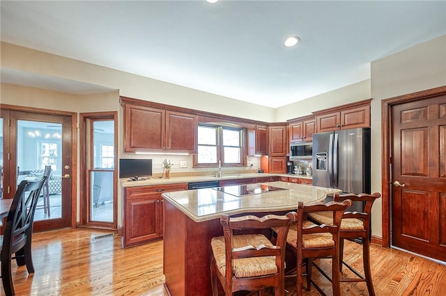 kitchen featuring a center island, light stone counters, light wood-type flooring, and black appliances