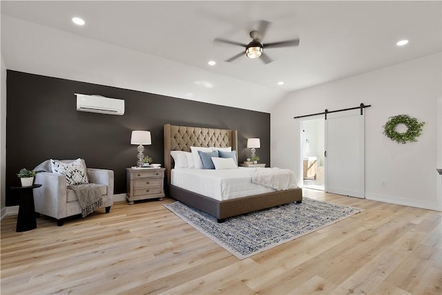 bedroom featuring lofted ceiling, an AC wall unit, light hardwood / wood-style floors, and a barn door