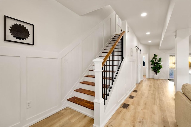 stairs with a barn door and hardwood / wood-style floors