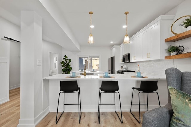 kitchen featuring a kitchen breakfast bar, a barn door, white cabinets, and appliances with stainless steel finishes