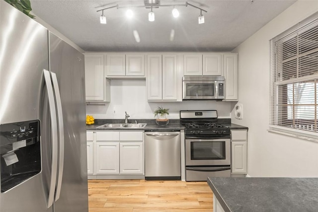 kitchen with sink, light hardwood / wood-style flooring, appliances with stainless steel finishes, a textured ceiling, and white cabinets