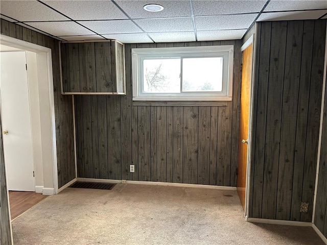 carpeted empty room featuring a paneled ceiling and wood walls