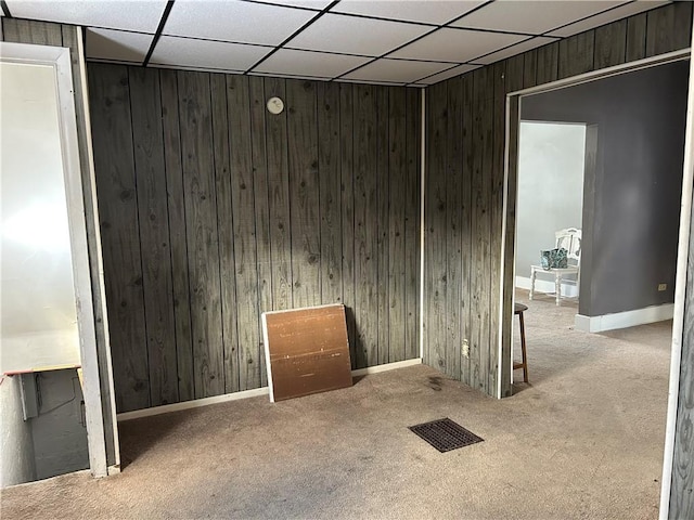 spare room with a paneled ceiling, light colored carpet, and wood walls