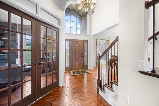 entrance foyer with a towering ceiling, hardwood / wood-style floors, a notable chandelier, and french doors