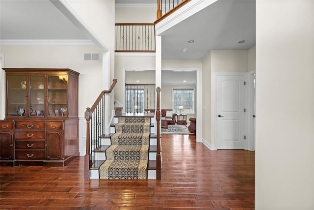 stairway featuring a high ceiling, wood-type flooring, and crown molding