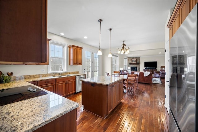 kitchen with sink, light stone counters, decorative light fixtures, a center island, and stainless steel appliances