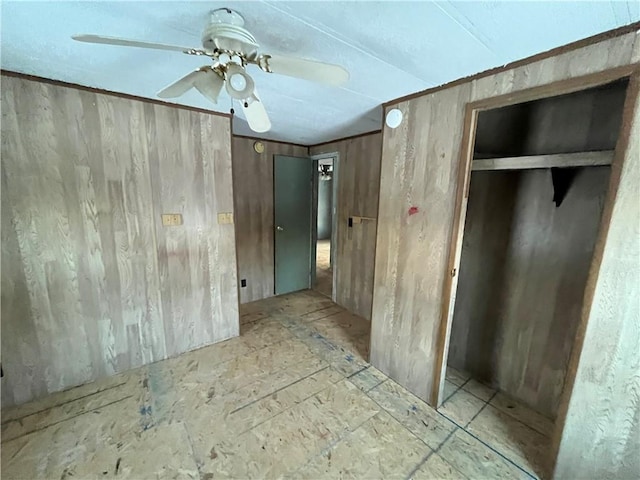 unfurnished bedroom featuring ceiling fan, wooden walls, and a closet