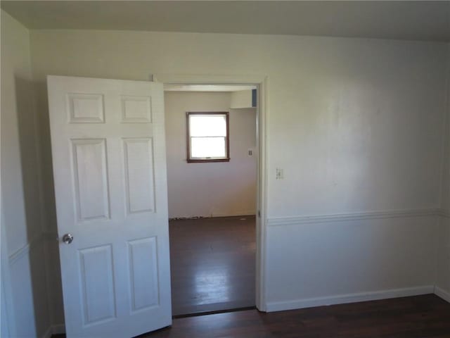 spare room featuring baseboards and dark wood-type flooring