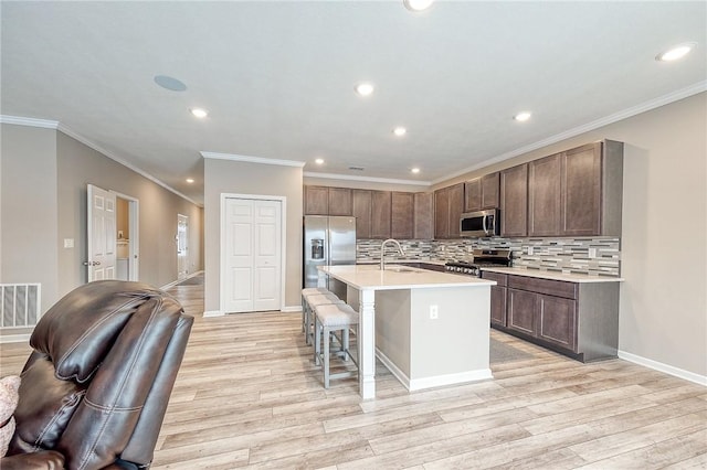 kitchen with appliances with stainless steel finishes, an island with sink, sink, a kitchen bar, and light hardwood / wood-style floors