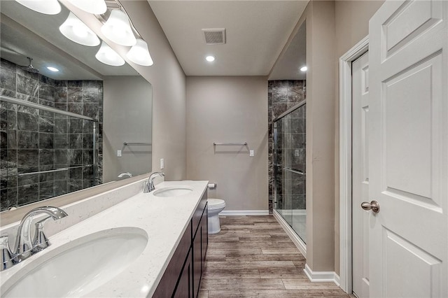 bathroom with wood-type flooring, toilet, vanity, and a shower with shower door