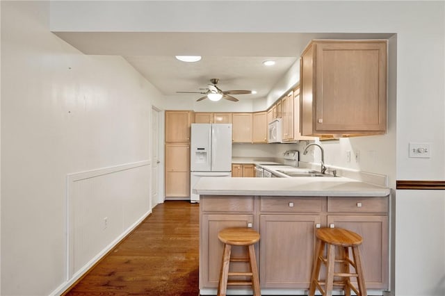 kitchen with a breakfast bar, sink, light brown cabinets, dark hardwood / wood-style flooring, and white appliances