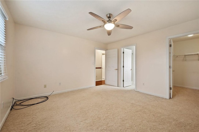 unfurnished bedroom featuring a spacious closet, light colored carpet, a closet, and ceiling fan