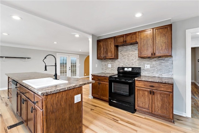 kitchen featuring sink, decorative backsplash, a kitchen island with sink, black range with electric stovetop, and french doors