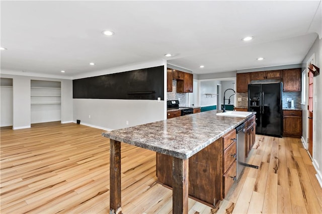 kitchen with sink, tasteful backsplash, black appliances, an island with sink, and light wood-type flooring