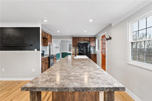 kitchen with a breakfast bar area, a center island, light hardwood / wood-style flooring, decorative backsplash, and black appliances