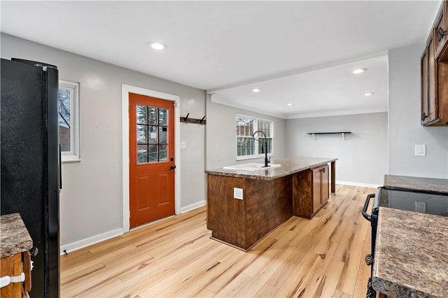 kitchen featuring light hardwood / wood-style flooring, sink, a center island with sink, and black appliances