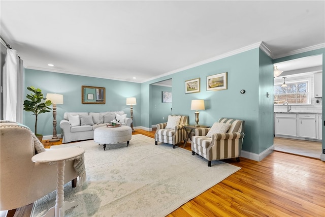 living room with ornamental molding, sink, and light wood-type flooring