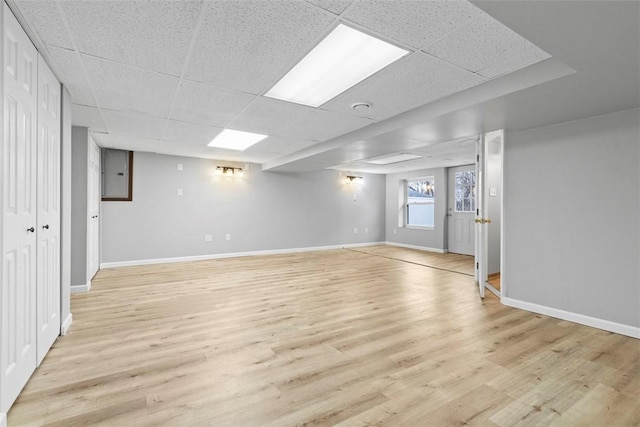 basement with a drop ceiling, electric panel, and light wood-type flooring