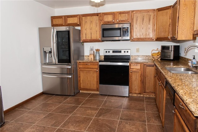 kitchen with light stone counters, appliances with stainless steel finishes, dark tile patterned flooring, and sink