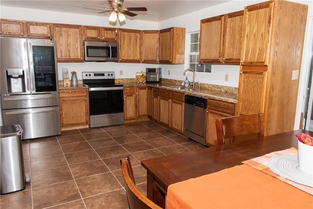 kitchen with sink, dark tile patterned flooring, dark stone counters, ceiling fan, and stainless steel appliances