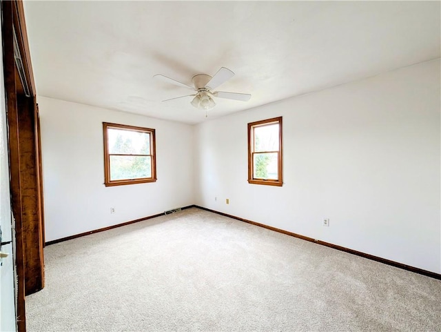 empty room featuring ceiling fan, light colored carpet, and plenty of natural light