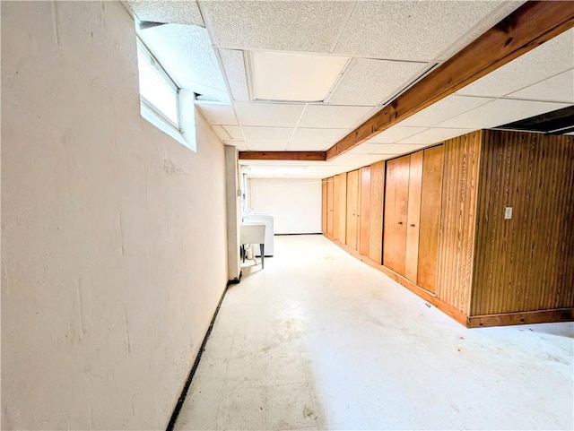 basement featuring a paneled ceiling, wooden walls, and washer / dryer