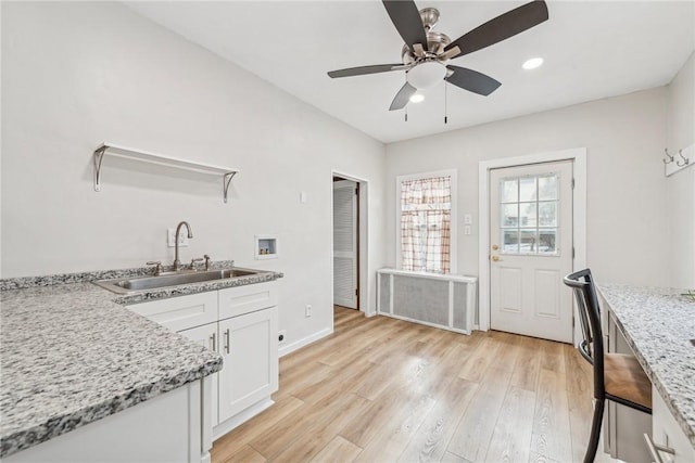 kitchen featuring radiator, a sink, light wood finished floors, ceiling fan, and white cabinets
