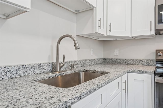 kitchen with electric range, white cabinets, a sink, and light stone countertops
