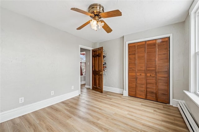 unfurnished bedroom featuring a closet, light wood finished floors, baseboards, a baseboard radiator, and a ceiling fan