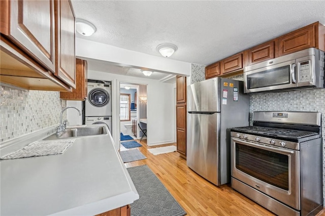 kitchen with stacked washer and clothes dryer, brown cabinets, appliances with stainless steel finishes, a sink, and light wood-type flooring