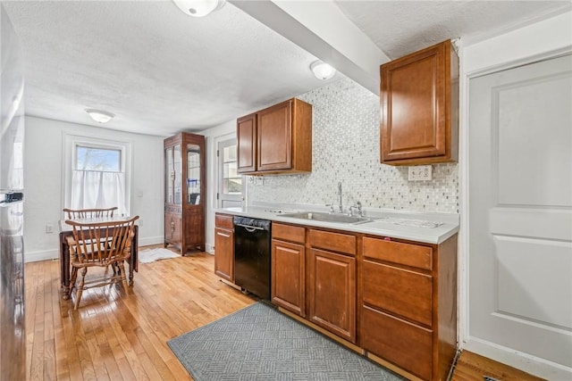 kitchen with light countertops, dishwasher, brown cabinets, a sink, and light wood-style floors