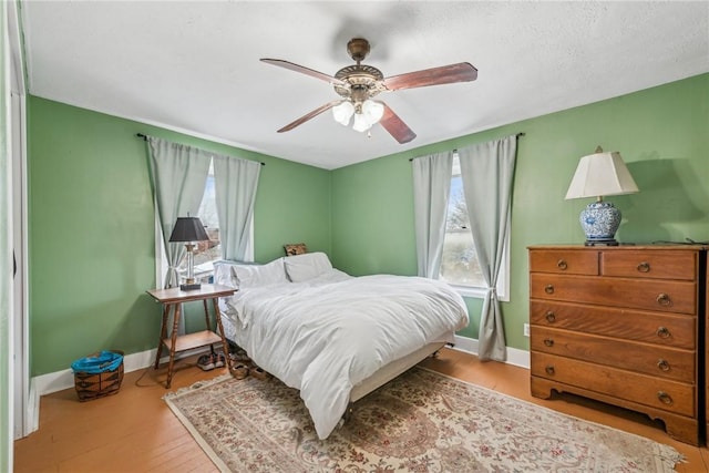 bedroom featuring a ceiling fan, baseboards, multiple windows, and wood finished floors