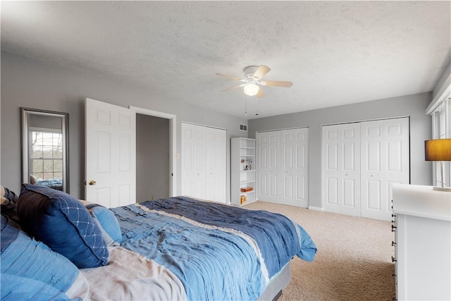 carpeted bedroom featuring ceiling fan, two closets, and a textured ceiling