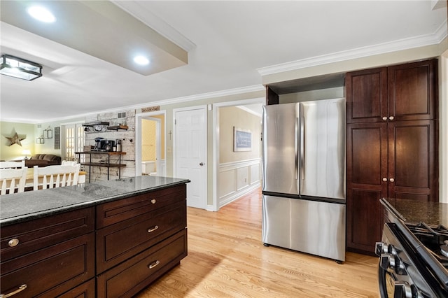 kitchen featuring crown molding, stainless steel appliances, light hardwood / wood-style floors, and dark stone countertops